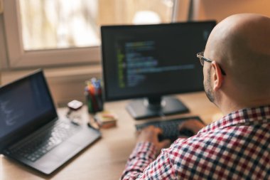 Ofiste çalışan erkek programcı, masasında oturuyor ve kodluyor.