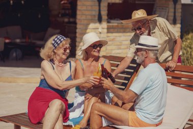 Bir grup kıdemli arkadaş yüzme havuzunda güneşlenip dinlenirken yaz tatilinde kadeh kaldırıyor, kokteyl ve bira içiyor ve eğleniyorlar. 