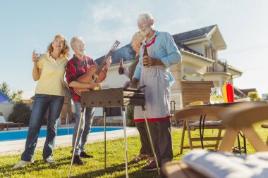 Bir grup neşeli son sınıf öğrencisi havuz başında barbekü partisi veriyor, ızgaranın etrafında toplanıp gitar çalıyor, şarkı söylüyor, et pişiriyor ve eğleniyorlar.