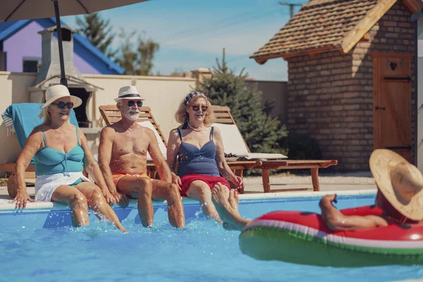 Group of elderly people having fun spending hot sunny summer day at the swimming pool, sunbathing and splashing water on each other, cooling down and relaxing while on a vacation