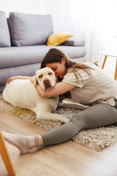 Beautiful young woman stretching out after exercising at home with her pet dog by her side, hugging and cuddling him
