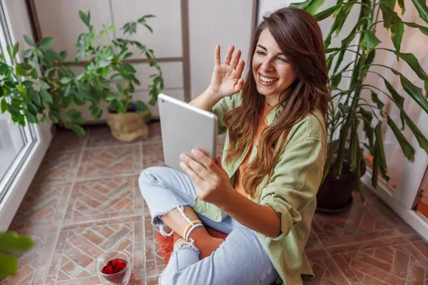 自宅でリラックスして過ごす女性 バルコニーフロアに座って紅茶を飲んで タブレットコンピュータを使って友人とビデオ通話をする — ストック写真