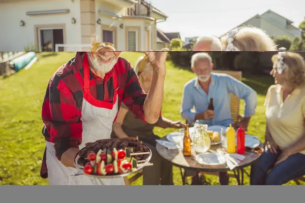 Elderly man serving food on a tray while having an outdoor lunch with friends in the backyard by the swimming pool