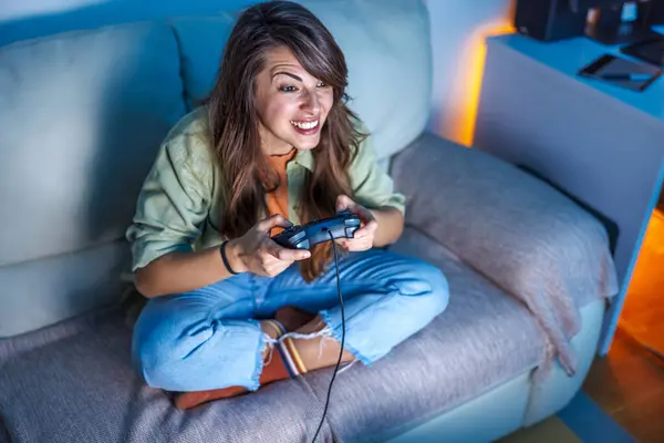 High angle view of beautiful young woman having fun playing video games at home late at night, relaxing and enjoying leisure time at home in the evening