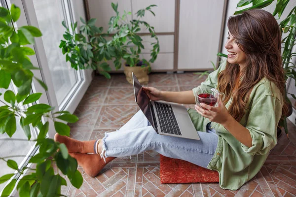 彼女のバルコニーに座っている美しい若い女性は ラップトップコンピュータを使用して自宅から遠隔操作し お茶を飲む — ストック写真