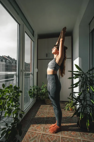 Woman in sportswear exercising at home in the morning, holding warrior one pose while doing yoga