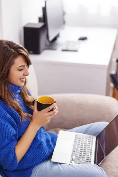 年轻女性坐在客厅沙发上 膝上抱着笔记本电脑 在家工作时喝咖啡休息的高视角画面 — 图库照片