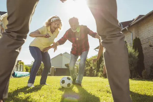 バックヤードの芝生でフットボールを楽しんだアクティブな高齢者のグループ 屋外で晴れた夏の日を楽しんで ボールの後に走る — ストック写真
