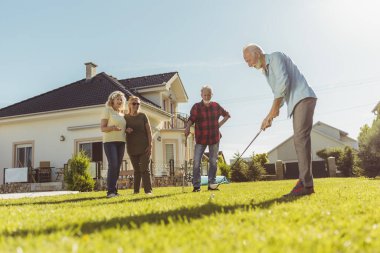 Aktif kıdemli arkadaşlar arka bahçede mini golf oynayıp güneşli yaz günlerini dışarıda geçiriyorlar.