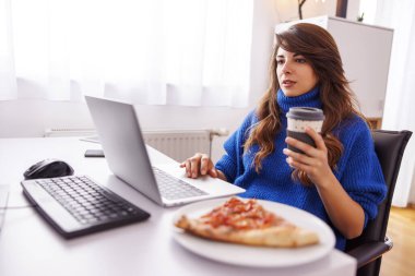 Ofisteki masasında oturan kadın programcı, evden kahve içip pizza yerken ara veriyor.