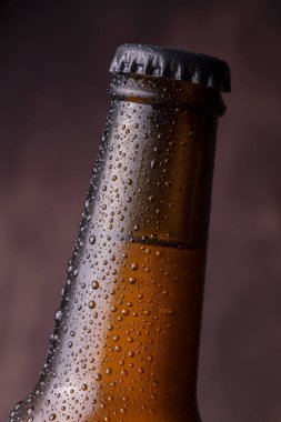 Bardağın yüzeyinde çiğ ve yoğunlaştırılmış su damlacıklarıyla birlikte soğuk, ıslak bira şişesi ayrıntıları.