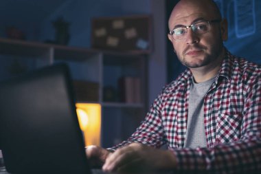 Erkek web tasarımcısı gece geç saatlere kadar bir ofiste dizüstü bilgisayar kullanarak çalışıyor.