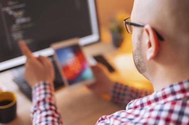 Tablet bilgisayarı olan bir ofiste çalışan ve kodlama sırasında masaüstü bilgisayarı kullanan bir erkek ağ geliştirici