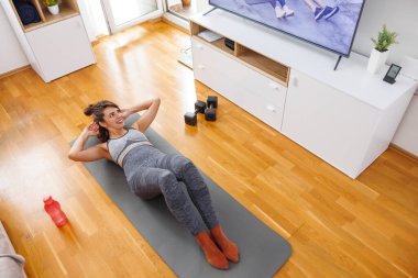 Spor giyim sektöründe aktif genç bir kadının internet üzerinden antrenman yaparken mekik çekişini yüksek açıdan izlemek.