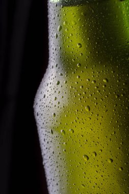 Bardağın yüzeyinde çiğ ve yoğunlaştırılmış su damlacıklarıyla birlikte soğuk, ıslak bira şişesi ayrıntıları.