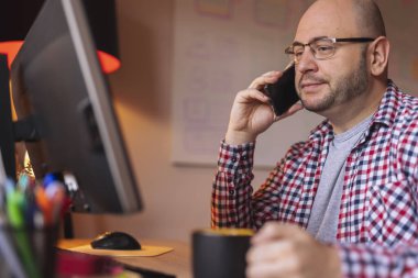 Ofiste çalışırken telefonla konuşan ve kahve içen bir adam.