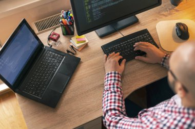 İç ofiste çalışan yazılım geliştiricisinin yüksek açılı görüntüsü, masasında oturması ve kodlaması; programcı evden uzaktan çalışıyor