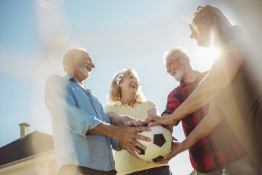 Bir grup neşeli, aktif son sınıf öğrencisi arka bahçedeki çimlerde futbol oynayıp güneşli bir yaz gününün tadını çıkarıyor ve maçtan önce futbol topunu bir arada tutuyorlar.