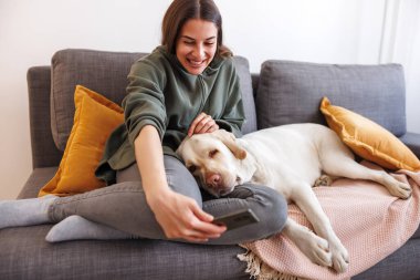Güzel genç bir kadın köpeğiyle selfie çekerken evde dinlenip eğlenirken eğleniyor.