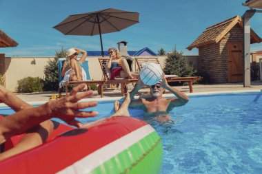 Yaz tatilinin tadını çıkaran iki son sınıf çifti. Erkekler havuzda voleybol oynarken kadınlar havuz kenarında güneşlenip kokteyl içiyorlar.