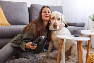 Genç bir kadın evcil hayvanıyla, güzel Labrador köpeğiyle, video oyunları oynayarak eğleniyor.