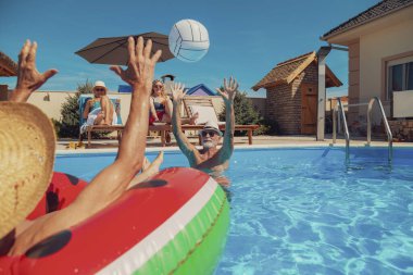 Yaz tatilinin tadını çıkaran iki son sınıf çifti. Erkekler havuzda voleybol oynarken kadınlar havuz kenarında güneşlenip kokteyl içiyorlar.