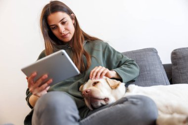 Güzel, genç bir kadın evde boş vakitlerin tadını çıkarıyor. Oturma odasındaki kanepede oturuyor ve yanında köpeği olan bir kitap okuyor.