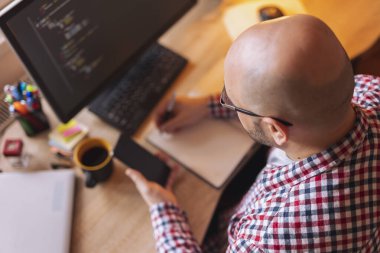 Dahili ofiste çalışırken akıllı telefon tutan ve planlama yapan yazılım geliştiricisinin yüksek açılı görünümü