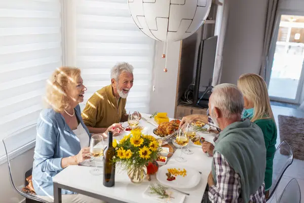 伝統的な夕食を一緒に家で感謝祭を祝いながら楽しんでいるシニアの人々のグループ — ストック写真