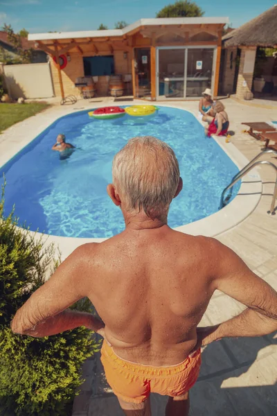Group of elderly friends relaxing and sunbathing by the swimming pool on a hot sunny summer day while on a vacation