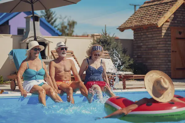 Group of elderly people having fun spending hot sunny summer day at the swimming pool, sunbathing and splashing water on each other, cooling down and relaxing while on a vacation