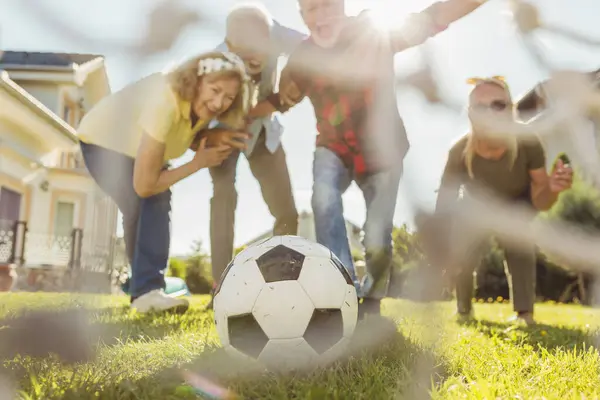 バックヤードの芝生でフットボールをするアクティブシニアのグループ 屋外で晴れた夏の日を楽しんで ゴールを獲得した後に祝う — ストック写真