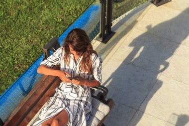 Evinin arka bahçesinde dinlenen, akıllı telefon kullanarak internette sörf yapan güzel bir kadının yüksek açılı görüntüsü.