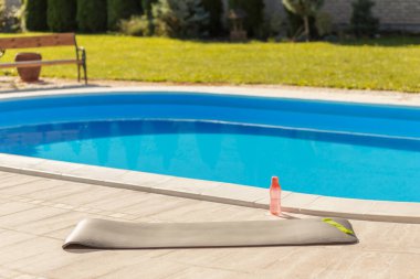 Yoga hasırı ve su şişesi yüzme havuzunun kenarına kurulmuş. Açık hava antrenmanı için hazır.