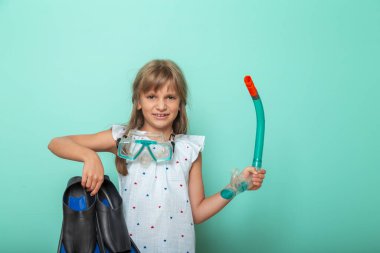 Heyecanlı küçük kız plaj tatiline hazırlanıyor. Elinde bir çift yüzgeç ve şnorkelli maske var.