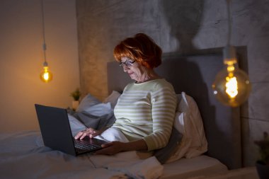 Güzel, son sınıf öğrencisi bir kadın gece yatağında yatarken dizüstü bilgisayarında aile üyeleriyle görüntülü konuşma yapıyor.