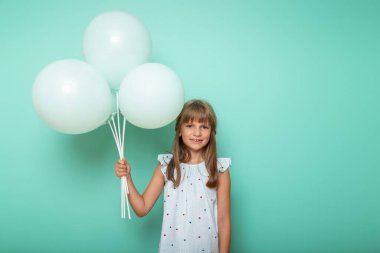 Elinde balonlarla gezen ve gülümseyen güzel bir kızın portresi. Nane rengi arka planda izole edilmiş ve fotokopi alanı olan.