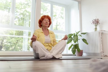 Yaşlı kadın evde meditasyon yaparak rahatlıyor - yaşlıların sağlıklı ve aktif yaşam tarzı konsepti