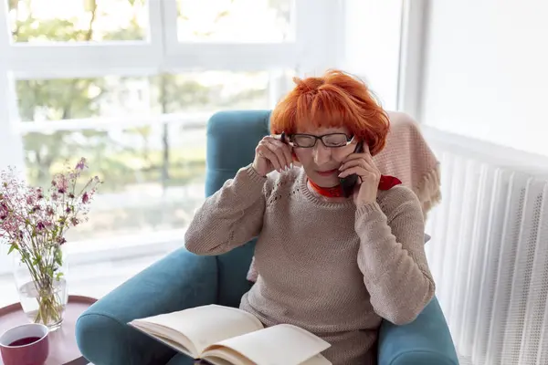 Starsza Kobieta Siedzi Fotelu Rozmawia Przez Telefon Pisze Planerze Relaksuje — Zdjęcie stockowe
