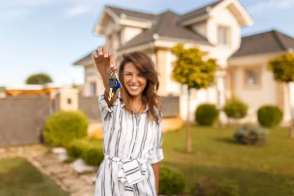 新しく購入した財産の鍵を握って 新しい家の前に立っている美しい若い女性 — ストック写真