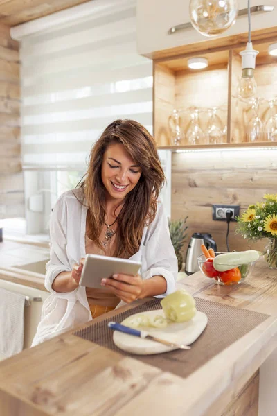 Beautiful young woman using a tablet computer in search for recipes while cooking