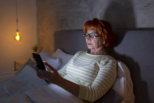 Starsza Kobieta Piżamie Siedząca Łóżku Korzystająca Smartfona — Zdjęcie stockowe