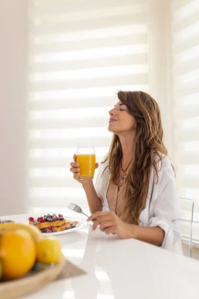Ung Kvinna Sitter Vid Middagsbordet Och Ler Dricker Färsk Apelsinjuice — Stockfoto