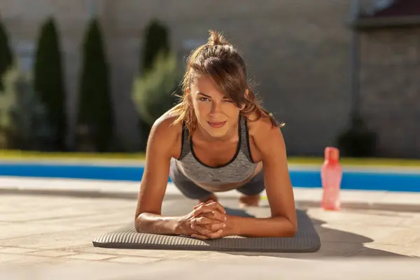 プールで屋外で働いている間 前腕プランク運動をしている若い女性にフィット — ストック写真