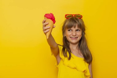 Çocuk bir külahta dondurma tutuyor ve gülümsüyor, sarı renkli arka planda izole edilmiş.