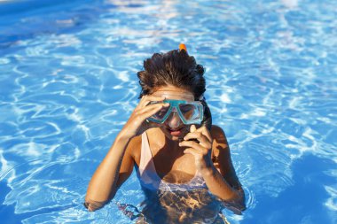 Güzel genç bir kadın yaz tatilinde şnorkel maskesini takıp yüzme havuzunda şnorkelle yüzerken eğleniyor.