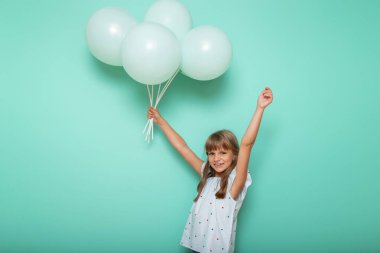 Güzel küçük bir kızın portresi. Elinde bir sürü balonla oynuyor ve gülümsüyor. Nane rengi arka planda izole edilmiş.