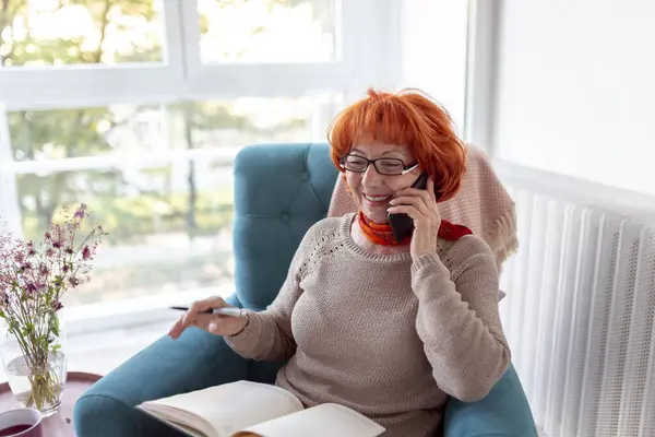 Senior Woman Sitting Armchair Speaking Phone Writing Planner Relaxing Home — Stock Photo, Image