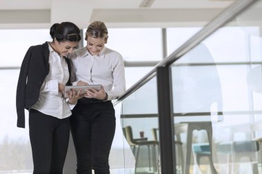 İki iş arkadaşı kahve molasında modern ofis koridorunda duruyor.