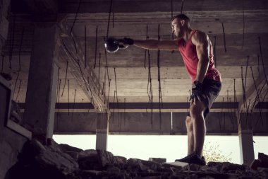 Genç, kaslı, atletik yapılı bir adamın, terkedilmiş bir binada ağırlık kaldırışının yan görüntüsü.